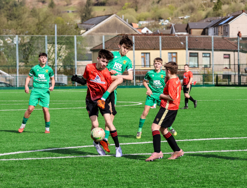 Youth football match with players in red and green kits competing for the ball.