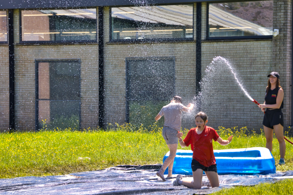 Children playing in a water slide, with one spraying water and others enjoying the fun.