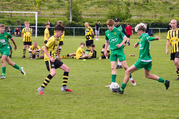 Boys in green and yellow jerseys playing football on a grass pitch.
