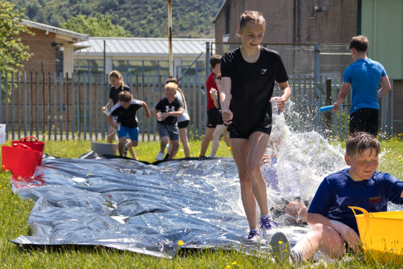 Children playing on a water slide outdoors, splashing and having fun in the sun.