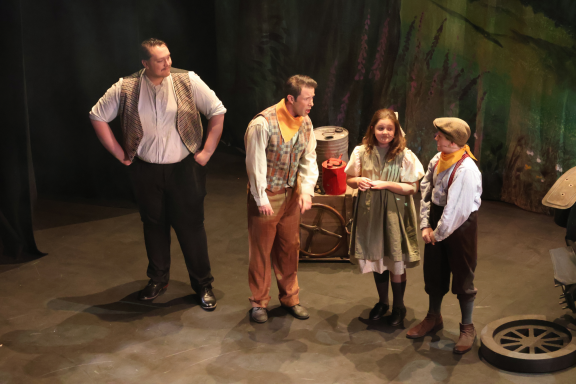 Four performers on stage in a theatrical scene, dressed in period costumes.