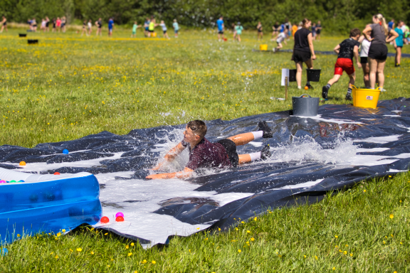 Children play on a water slide in a field, splashing water and enjoying summer fun.