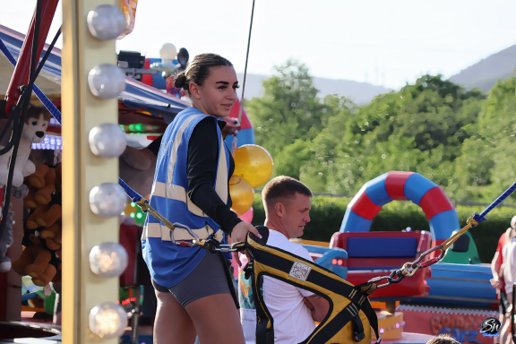 A woman in a blue top operates a fairground ride with a man nearby.