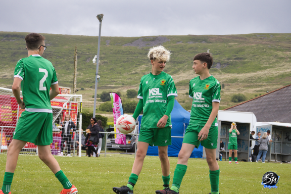 Two young football players in green kits chatting on a grassy field.