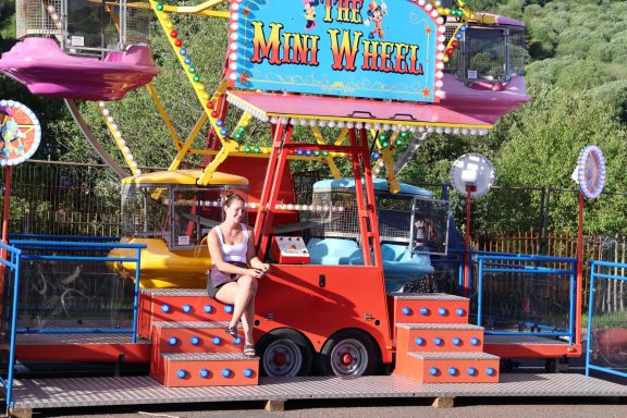 A girl sitting on a brightly coloured mini Ferris wheel attraction.