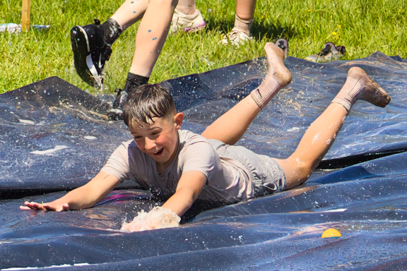 Child slides on a water-covered surface, enjoying a sunny day outdoors.