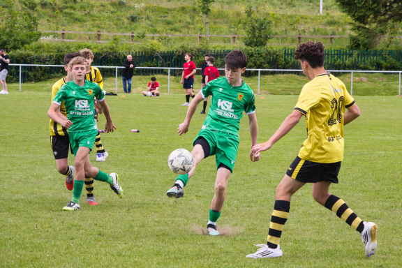 Boys playing football on a grass pitch, wearing green and yellow kits.