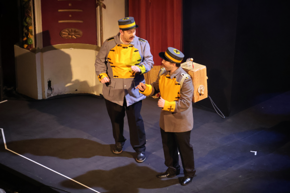 Two male performers in vintage uniforms engaging on stage.
