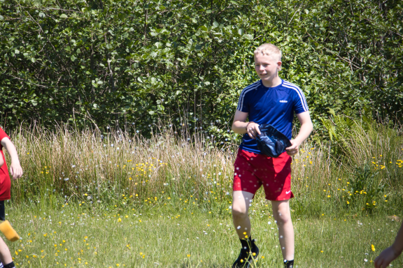 A boy in a blue shirt and red shorts plays outside in a grassy area.