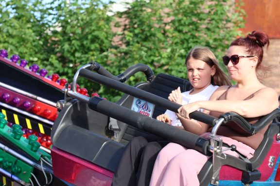 Two women sit in a ride with vibrant, multicoloured controls, looking focused.