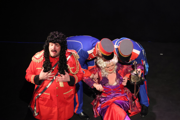 Performers in vibrant costumes engage in a theatrical scene on stage.