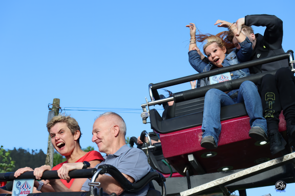 Four people enjoying a roller coaster ride with expressions of excitement and joy.
