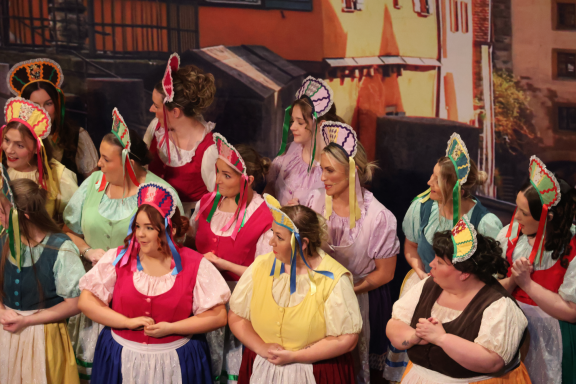 A group of women in colourful costumes with headdresses, performing on stage.
