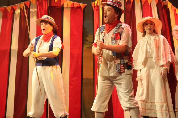 Three performers dressed in vintage circus attire singing on stage.