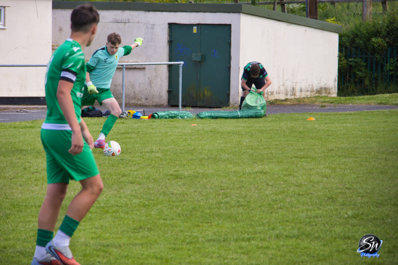Two football players in green kits on a grass pitch, one preparing to kick the ball.