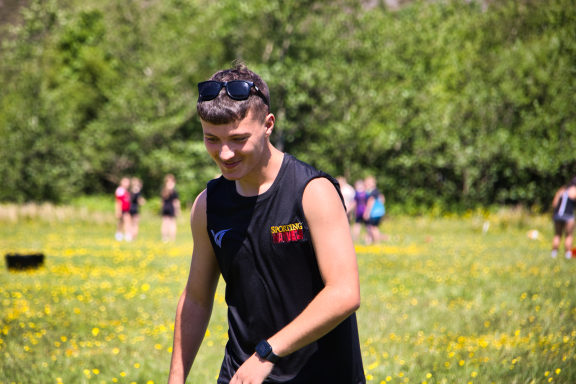 Young man in a black sleeveless top walking through a grassy field with flowers.