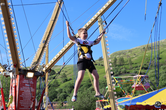 Child bouncing on a bungee trampoline at a funfair, with green hills in the background.