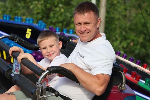 A man and a boy smiling while seated on a carnival ride.