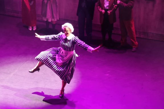 A performer dancing on stage in a flowing dress with purple lighting.