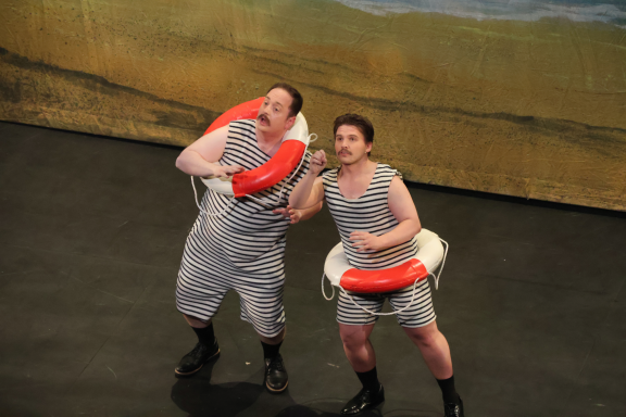 Two performers in grey outfits holding lifebuoys, singing on stage.