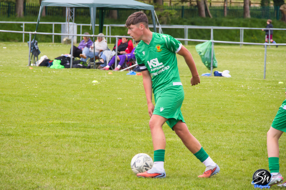 Young football player in green kit preparing to kick a ball on a grass pitch.