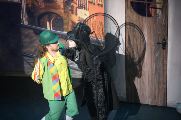 A performer in a colorful costume interacts with a character in a dark outfit.