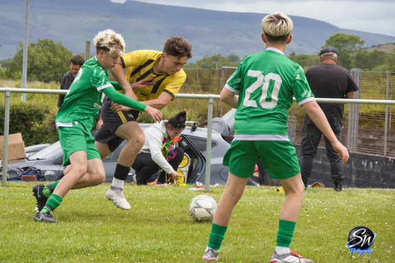 Two young football players in green kits compete for the ball against a player in a yellow kit.