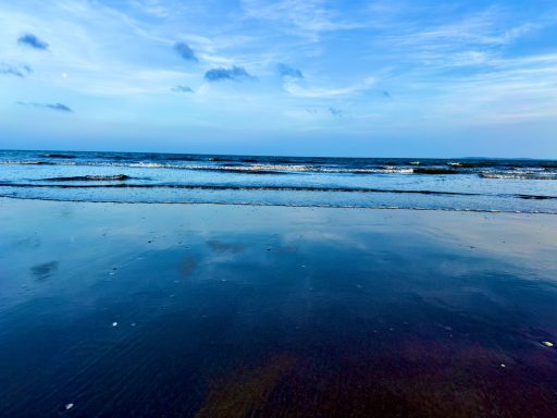 Calm ocean reflecting the sky, with gentle waves and distant clouds.