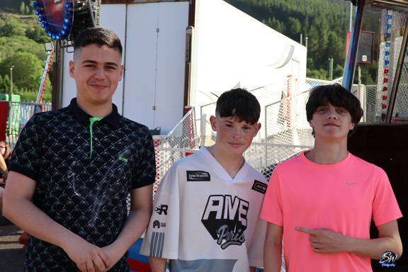 Three boys standing together at a fair, smiling and wearing casual clothing.