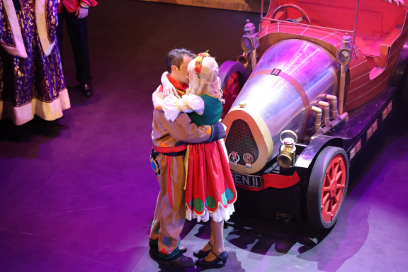A couple in festive costumes sharing a kiss beside a colourful vintage vehicle.