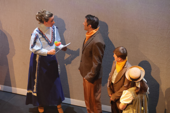 Four performers in period costumes engage in a theatrical scene.